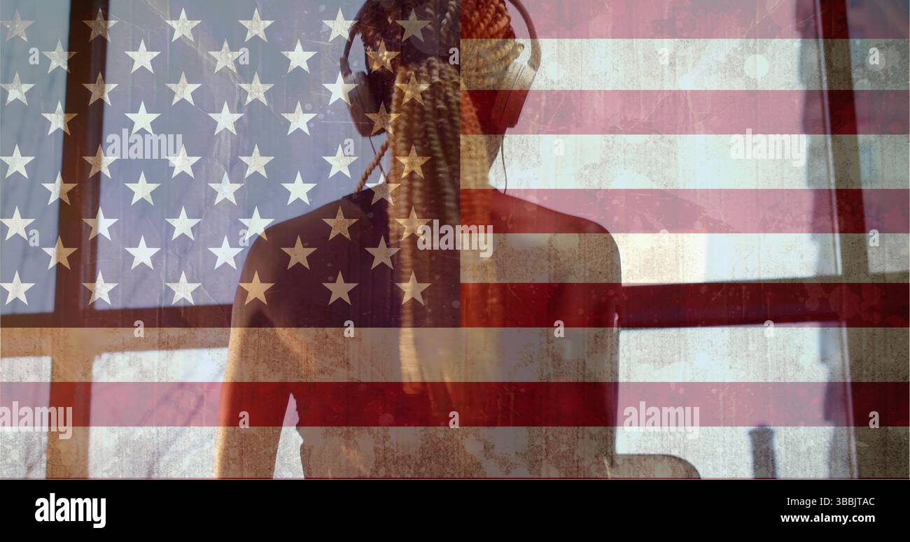 Femme debout portant un haut sans manches donnant sur la fenêtre de la chambre, avec écouteurs et revêtement du drapeau américain Banque D'Images