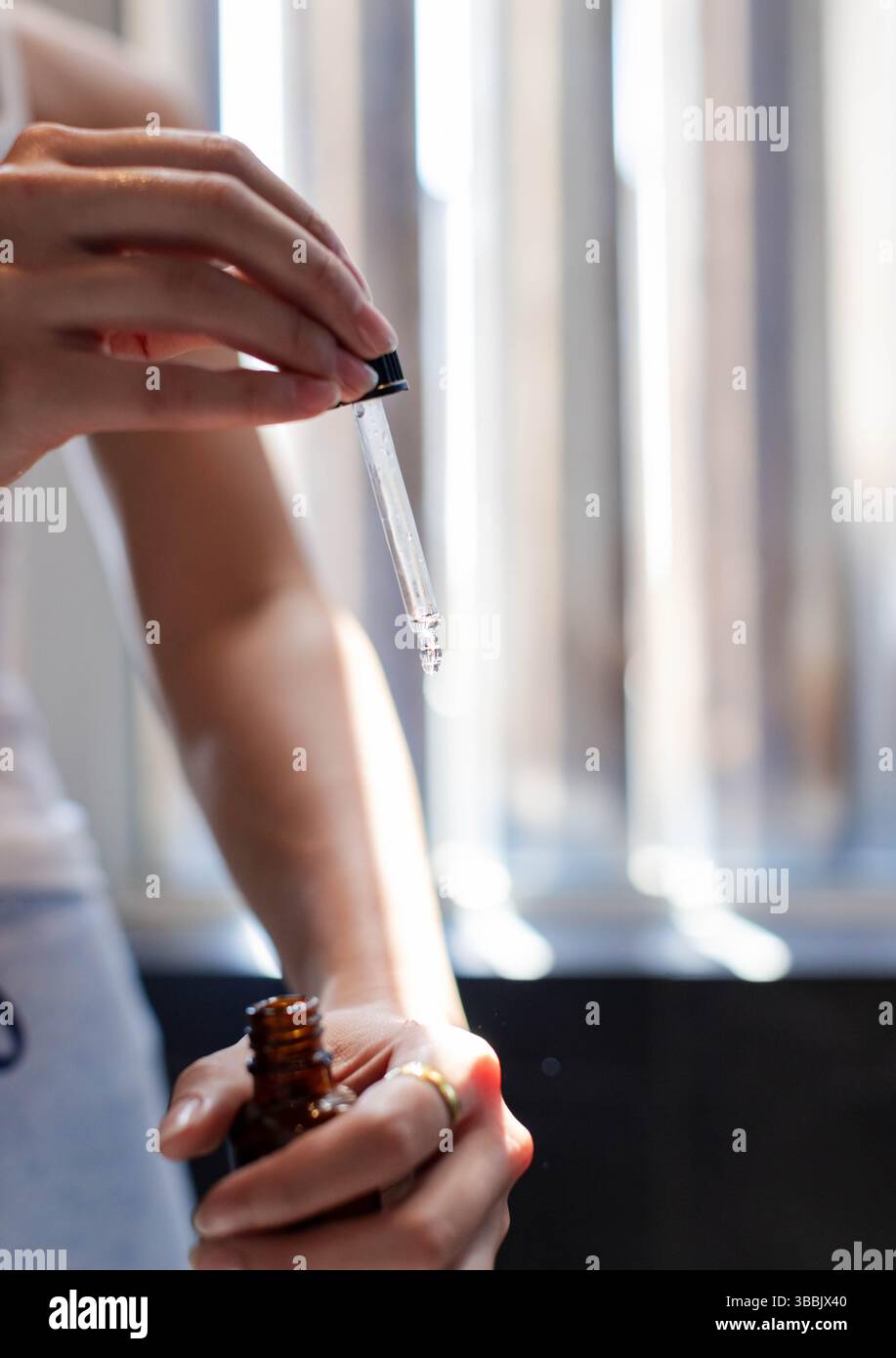 Femme asiatique appliquant le sérum sur l'avant-bras à la vanité de salle de bain, avec pipette compte-gouttes et bouteille ambre Banque D'Images