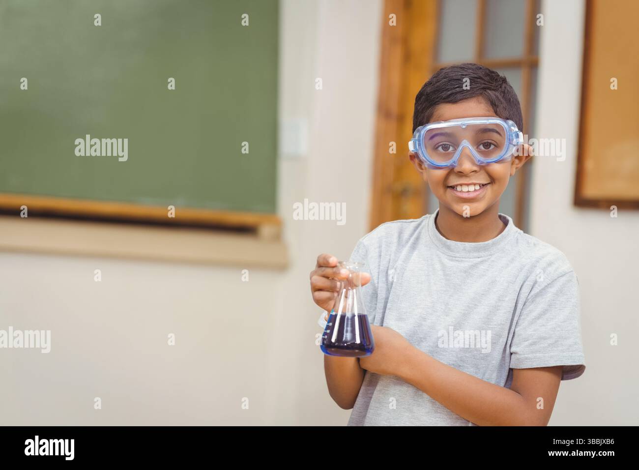 La fiole conique contenant du liquide bleu foncé repose sur le bureau de la classe, près du tableau vert Banque D'Images