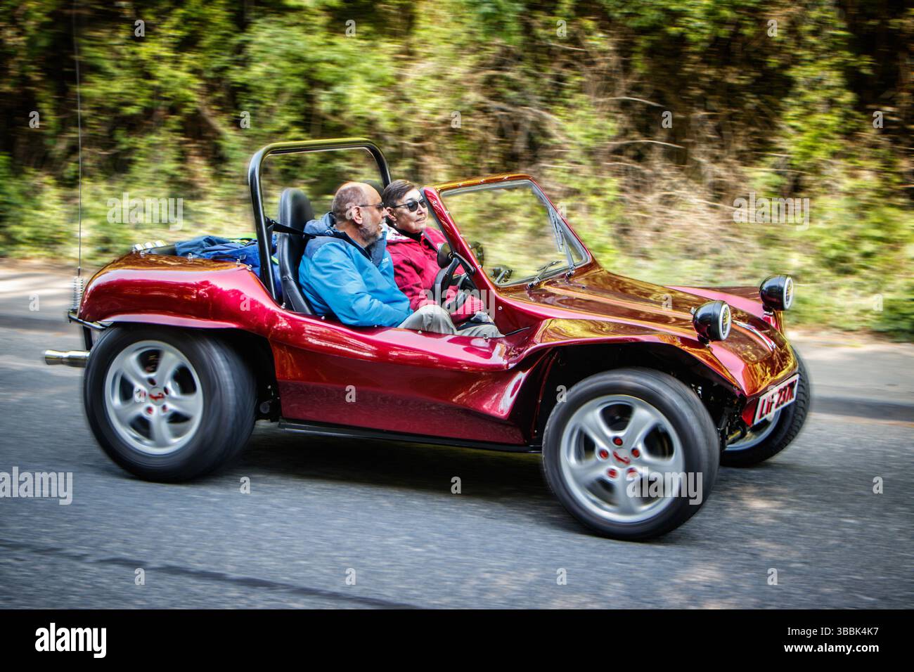 Deux personnes conduisant un buggy dune rouge brillant sur une route entourée de verdure par une journée ensoleillée Banque D'Images
