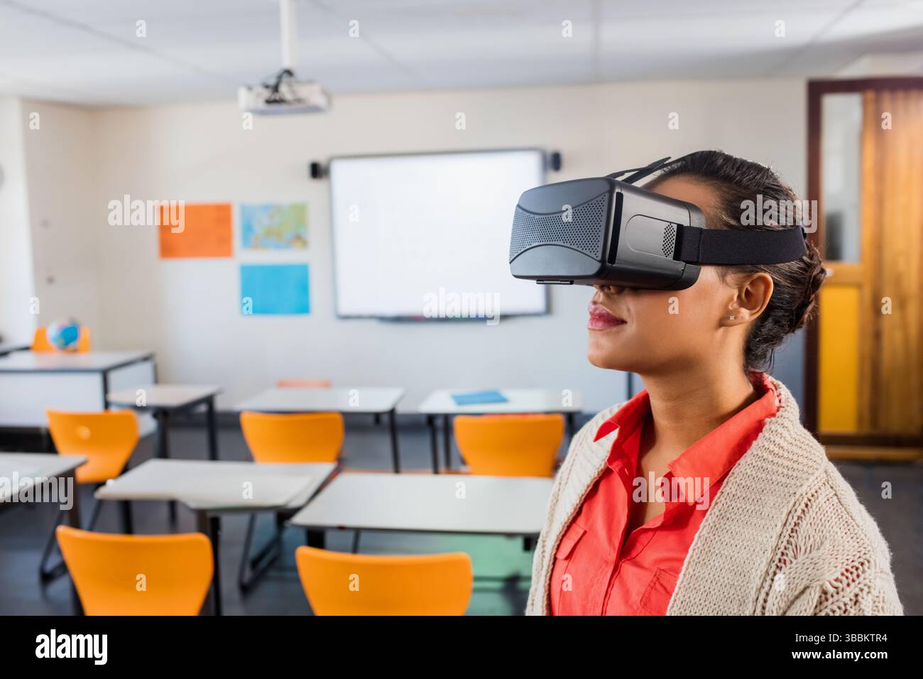 Casque de réalité virtuelle reposant sur un bureau blanc dans une salle de classe, avec des chaises orange, tableau blanc Banque D'Images