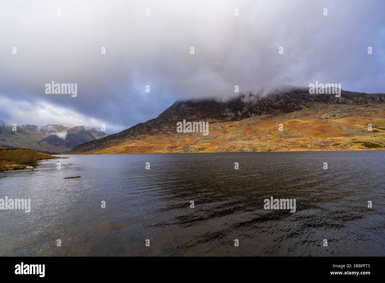Les eaux tranquilles de Llyn Ogwen baignent sous les pentes de Glyderau enveloppées de brume sous un couvert de nuages Banque D'Images