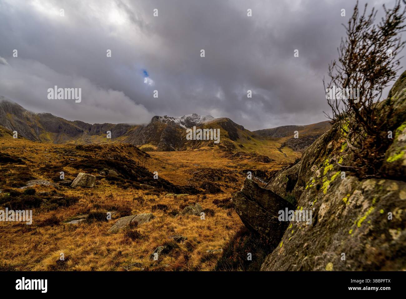 Couvant des pics poussiéreux de neige s'élevant au-dessus du cirque accidenté de Cwm Idwal sous des nuages de tempête changeants et des landes fauchées au premier plan Banque D'Images
