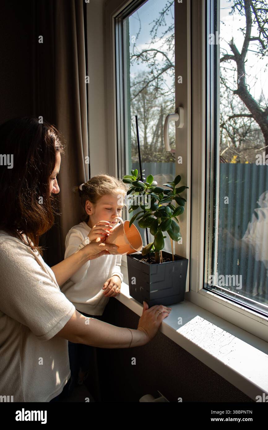 Mère enseigne à son enfant d'âge préscolaire comment arroser les plantes d'intérieur. Enfant impliqué dans l'activité familiale du ménage. Développement de la petite enfance Banque D'Images
