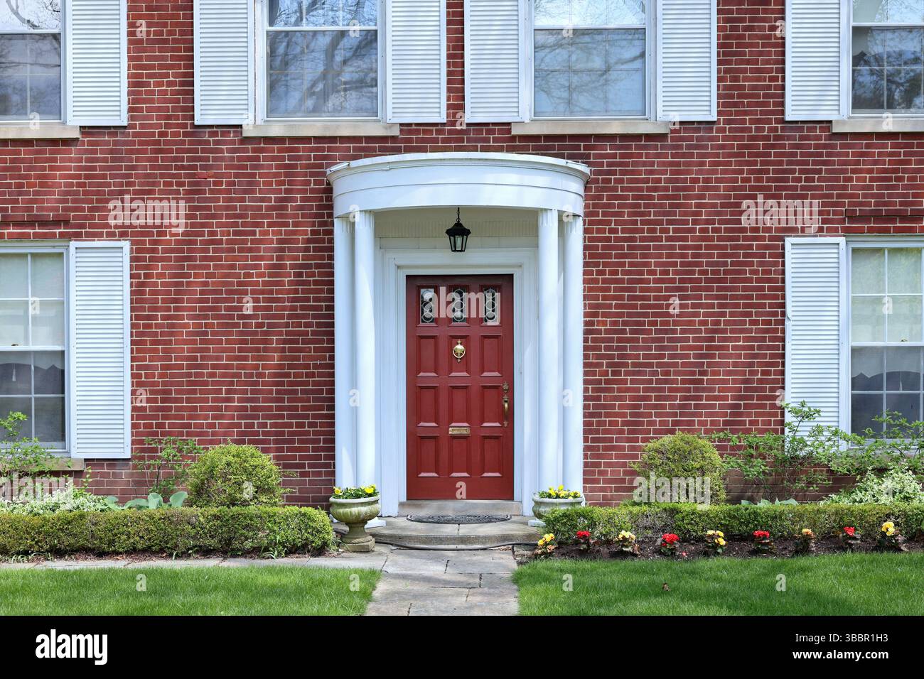 Devant la maison traditionnelle en brique de deux étages avec volets blancs Banque D'Images