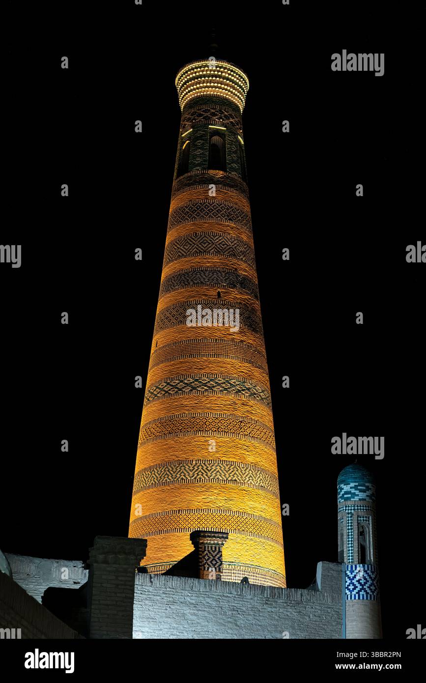 Islam Khodja Minaret à Khiva, Ouzbékistan brille chaleureusement la nuit, ses briques rayées et ses carreaux bleus illuminés contre le ciel sombre. Banque D'Images