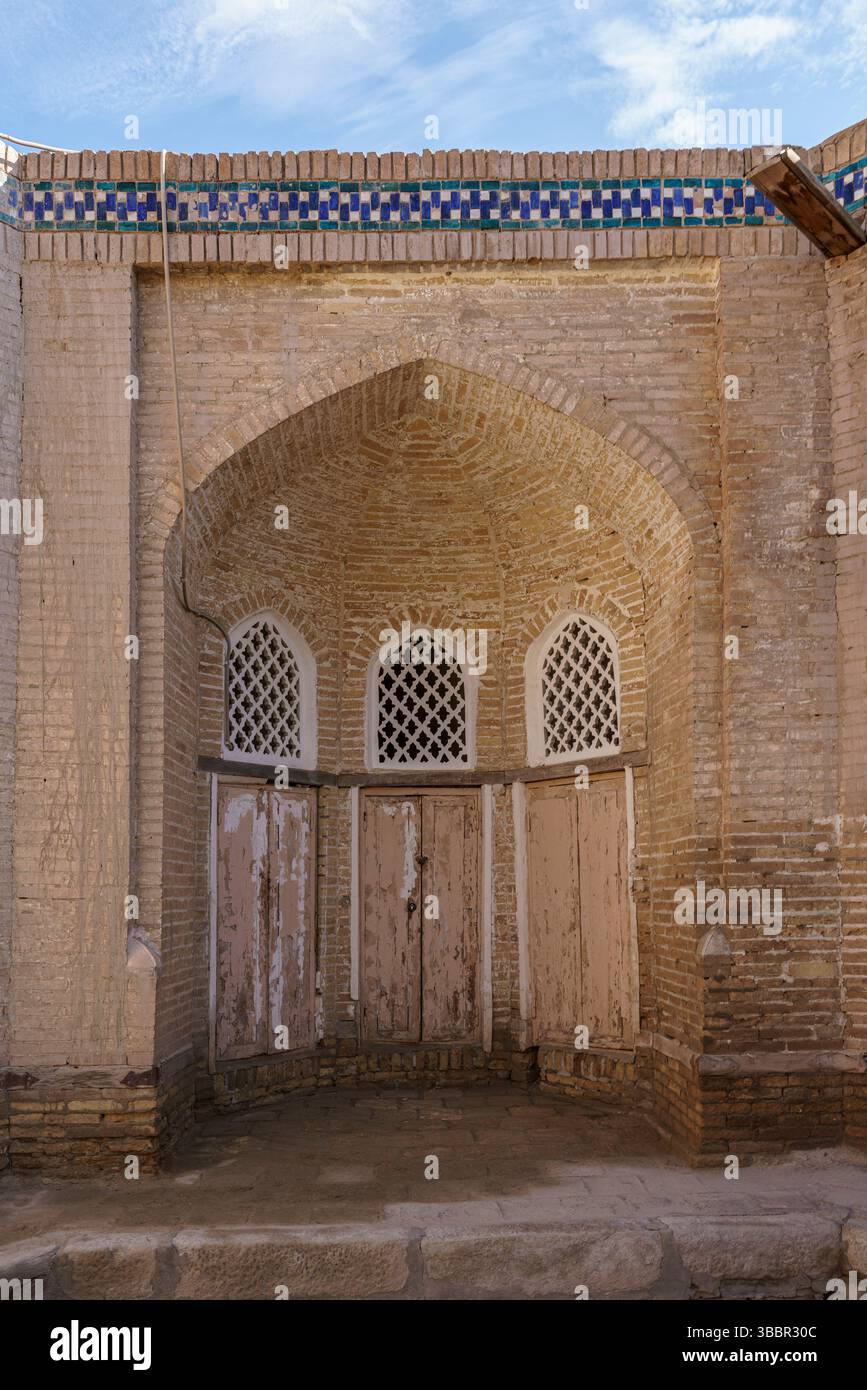 Une double porte en bois avec des fenêtres en treillis est située dans la façade en briques de sable de Islam Khoja Madrasah à Khiva, en Ouzbékistan. Banque D'Images