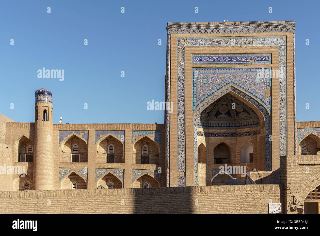 Une grande entrée en carrelage bleu avec une arche pointue marque Madrassah Alla Kouli Khan à Khiva Ouzbékistan avec des murs de sable et des tours jumelles. Banque D'Images