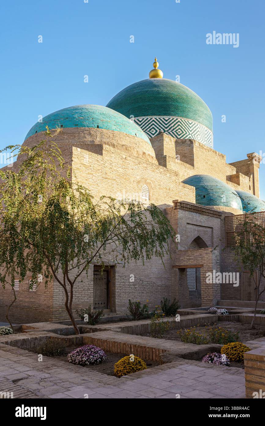 Un dôme turquoise et une entrée voûtée marquent le mausolée de Pahlavan Mahmud à Khiva Ouzbékistan avec des murs de sable et un arbre feuillu. Banque D'Images