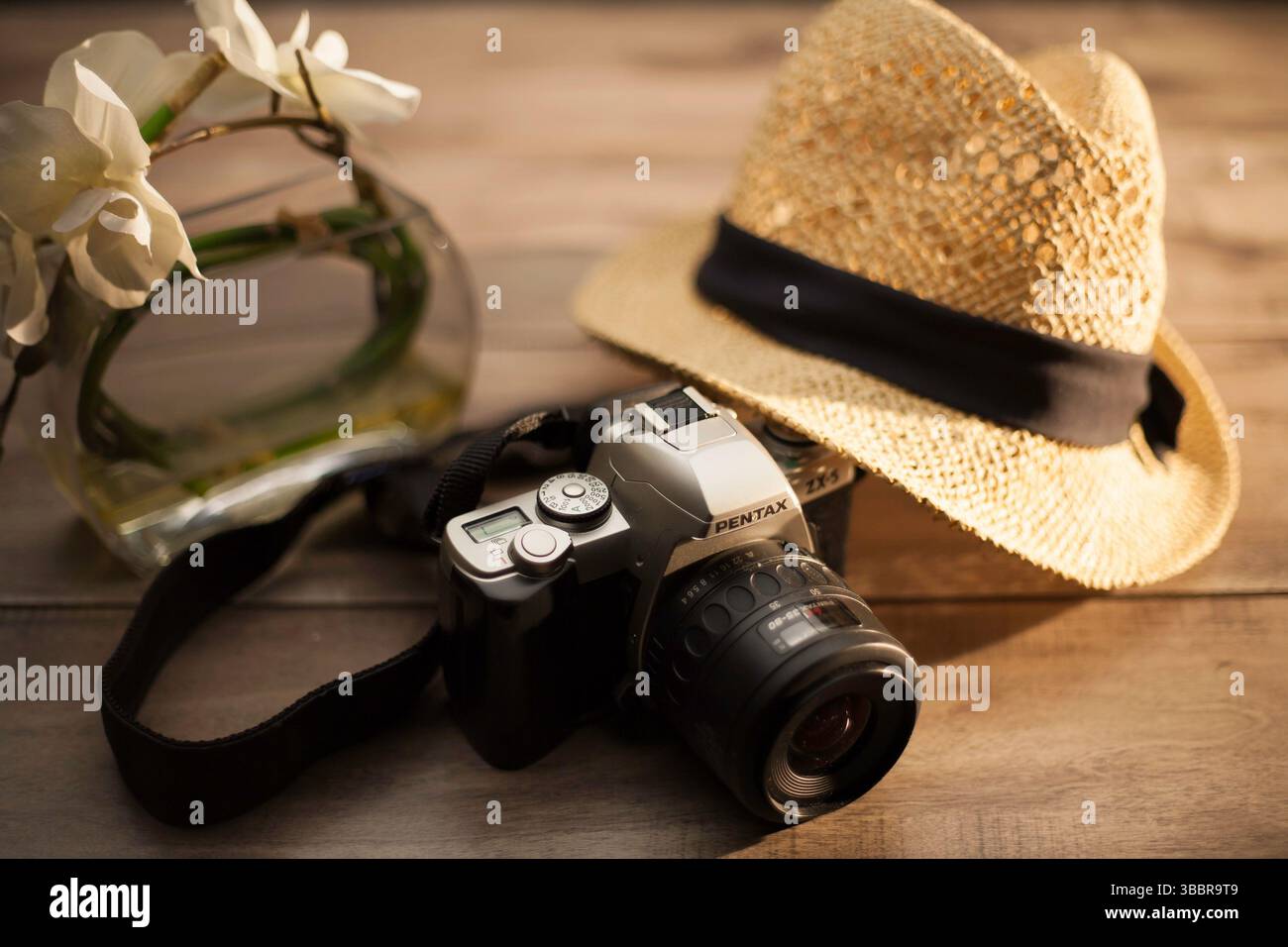 Appareil photo Pentax vintage, chapeau de paille et vase à fleurs sur table en bois évoquent une ambiance de voyage chaleureuse et nostalgique et l'amour pour la photographie et les moments paisibles. Banque D'Images
