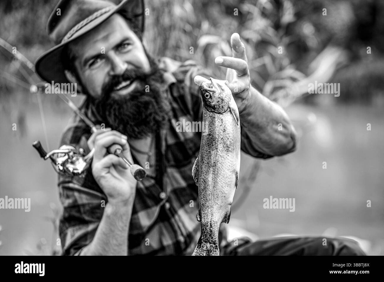 Pêcheur tenant des poissons, rivière de montagne en arrière-plan. Pêche. Pêche. Pêcheur et truite. Noir et blanc Banque D'Images
