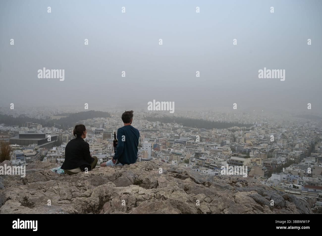 Athènes, Grèce, 16 mai 2025. Les visiteurs regardent au-dessus de la ville tandis qu'Athènes est couverte de nuages de poussière. Une épaisse couverture de poussière saharienne a balayé la capitale grecque vendredi, jetant de la brume sur la ville et suscitant des avertissements sanitaires de la part des autorités. Crédit : Dimitris Aspiotis/Alamy Banque D'Images