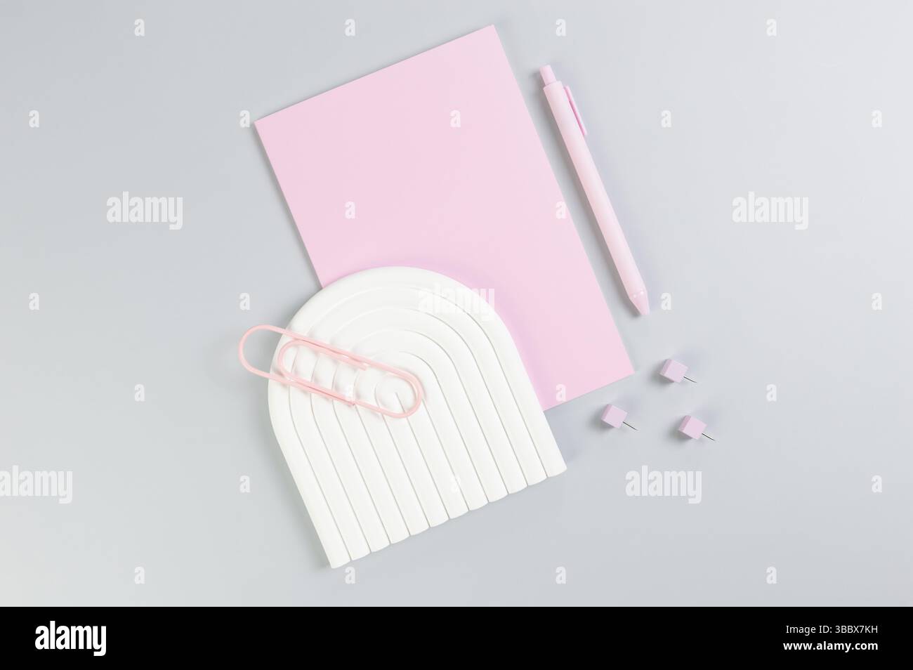 Vue de dessus du carnet rose, stylo rose, trombone, épingles, plateau à arc blanc sur fond gris. École, papier peint de bureau. Pose à plat, espace de copie. Banque D'Images