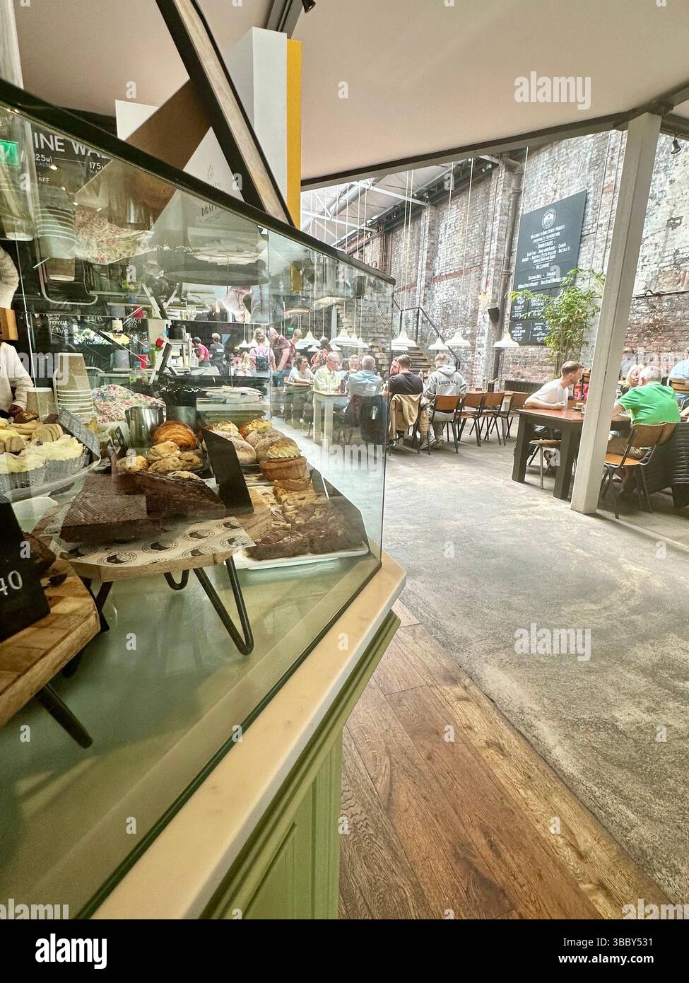 Vue de derrière la vitrine à pâtisseries au rez-de-chaussée du Duke Street Market, Liverpool, montrant l'intérieur industriel, les restaurants et les stands de nourriture. Éditorial - Image de stock capturée avec un smartphone