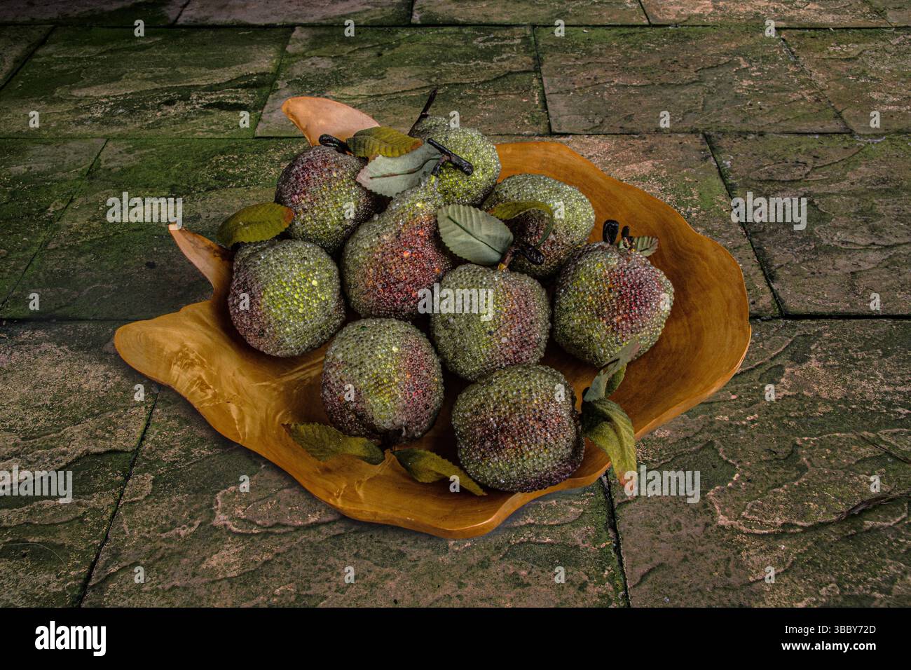Image de nature morte de pommes en verre ornementales dans un bol en bois sculpté à la main sur un patio de jardin pavé en pierre Banque D'Images
