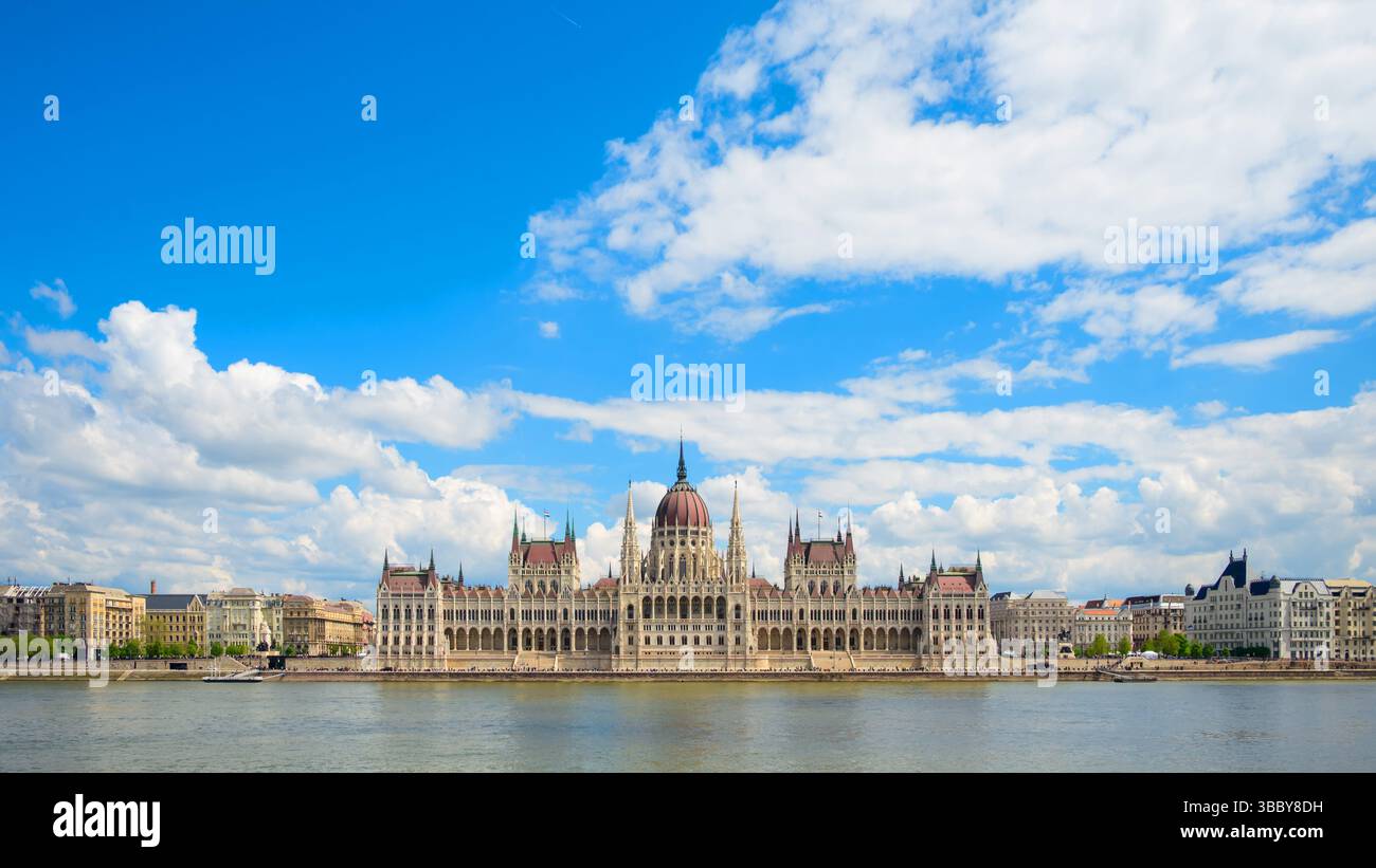 Les bâtiments du Parlement hongrois se dressent majestueusement le long du Danube à Budapest, sous un ciel bleu clair rempli de nuages. Il présente le Banque D'Images