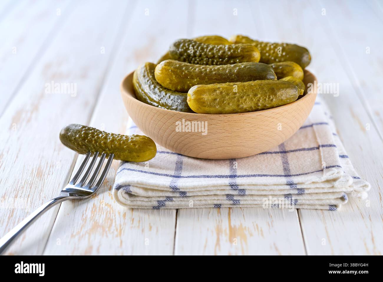 cornichons marinés dans un bol en bois sur une table de cuisine blanche, mise au point sélective. concombres fermentés savoureux dans un bol en bois sur une table blanche. Banque D'Images
