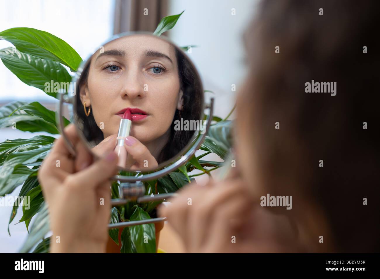 Femme appliquant du rouge à lèvres tout en regardant dans le miroir. Banque D'Images