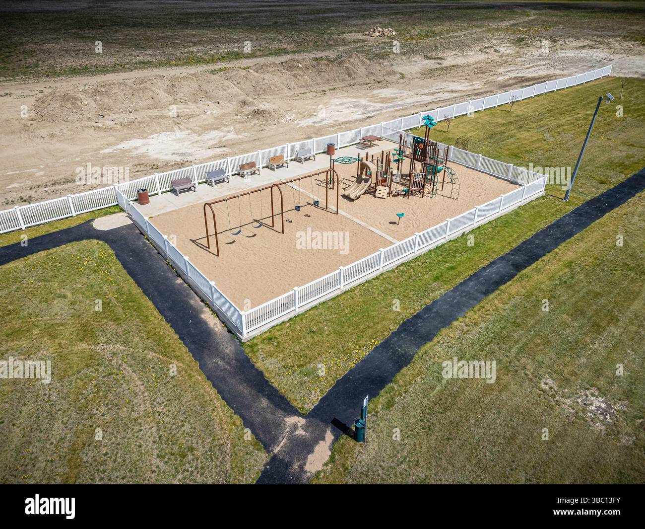 Parc avec aire de jeux et clôture. Le terrain de jeu possède un ensemble balançoire et une structure de jeu Banque D'Images