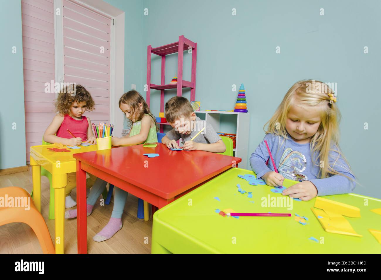 Les adorables enfants d'âge préscolaire s'assoient aux bureaux de la salle de jeux et dessinent avec des crayons de couleur Banque D'Images
