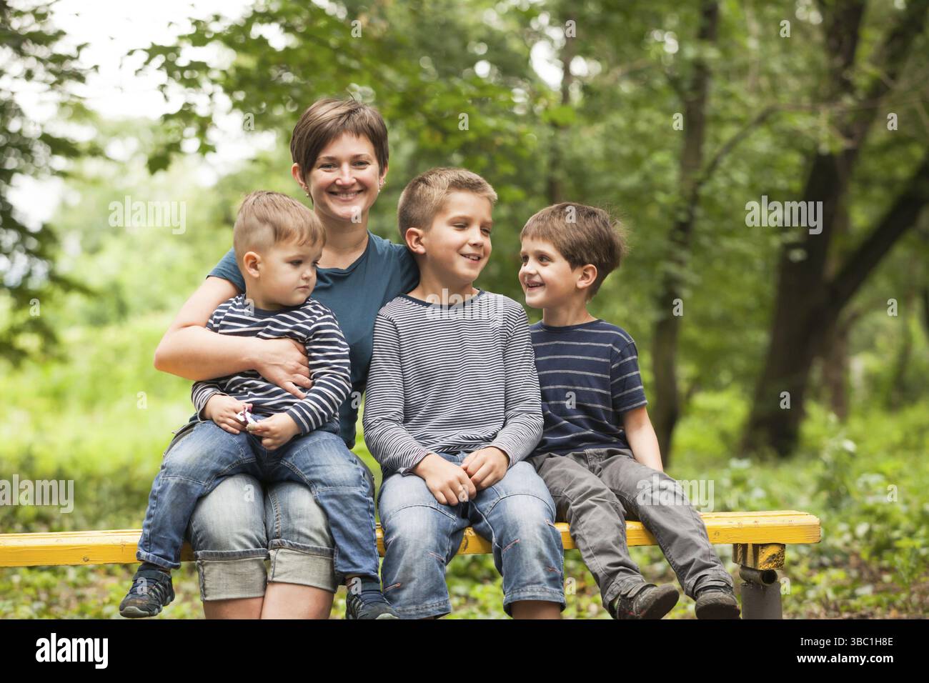 Mère jouant avec ses trois fils sur un banc de parc Banque D'Images