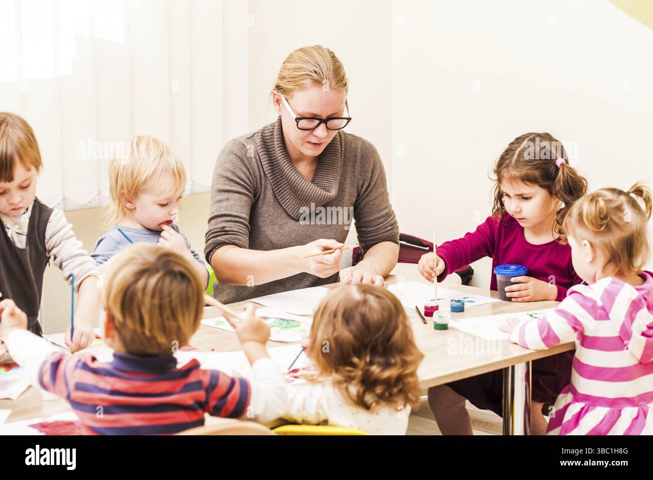 Les enfants et le tuteur sont la peinture à l'aide d'un pinceau et d'aquarelles sur papier dans le jardin d'enfants Banque D'Images