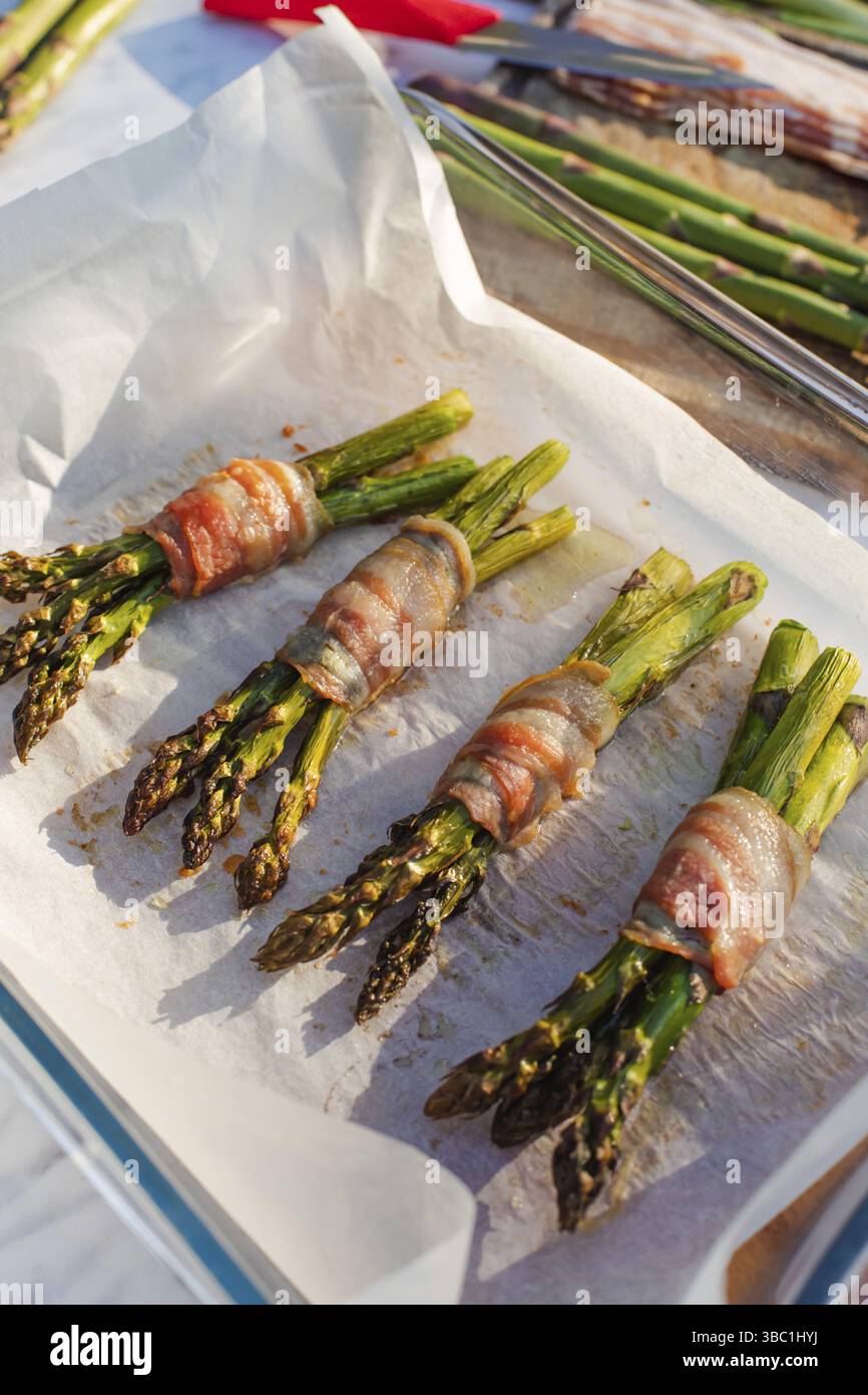Des asperges appétissantes enveloppées de bacon frais se trouvent sur du papier. Les asperges avec du bacon sur la table à l'extérieur Banque D'Images Des asperges appétissantes enveloppées de bacon frais se trouvent sur du papier. Les asperges avec du bacon sur la table à l'extérieur Banque D'Images