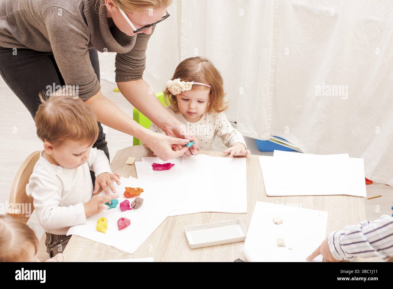 L'enseignant aide le jeune fille de faire une figure de la pâte à modeler sur la table Banque D'Images