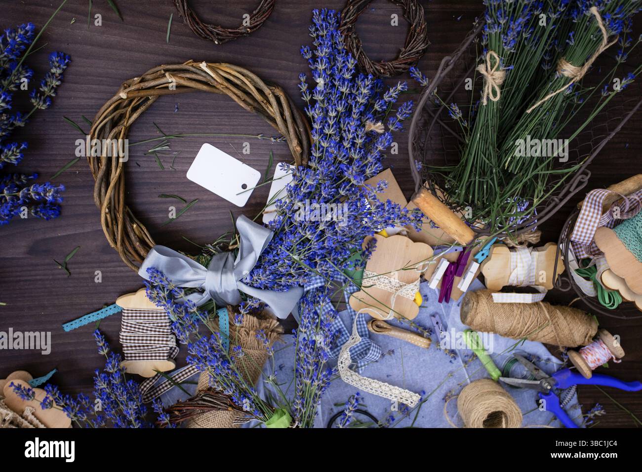 Vue de dessus couronne faite à la main décorée de fleurs de lavande sur une surface en bois. Variété de matériaux et d'outils pour fleurs faites à la main. Bouquet d'aromati frais Banque D'Images