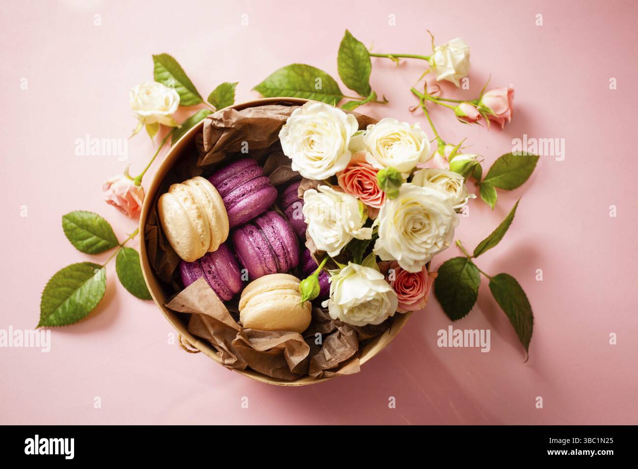 Vue de dessus d'une boîte ronde remplie de délicieux macarons blancs et violets, décorés de roses. Boîte cadeau Sweet. Fond rose Banque D'Images