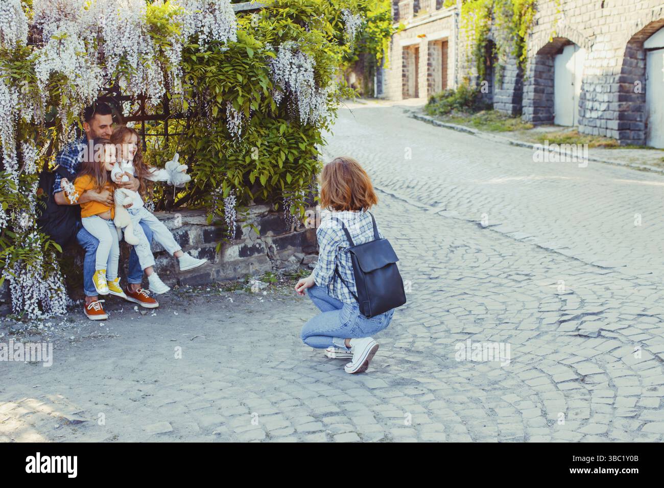 Belle et pleine d'amour famille avec deux enfants, photo en plein air sur une vieille rue pavée. Mère assise sur ses haunches regardant sa famille sous Gly Banque D'Images