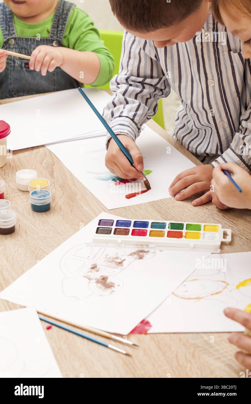 Les enfants apprennent à peindre avec un pinceau et des aquarelles sur papier à la maternelle Banque D'Images