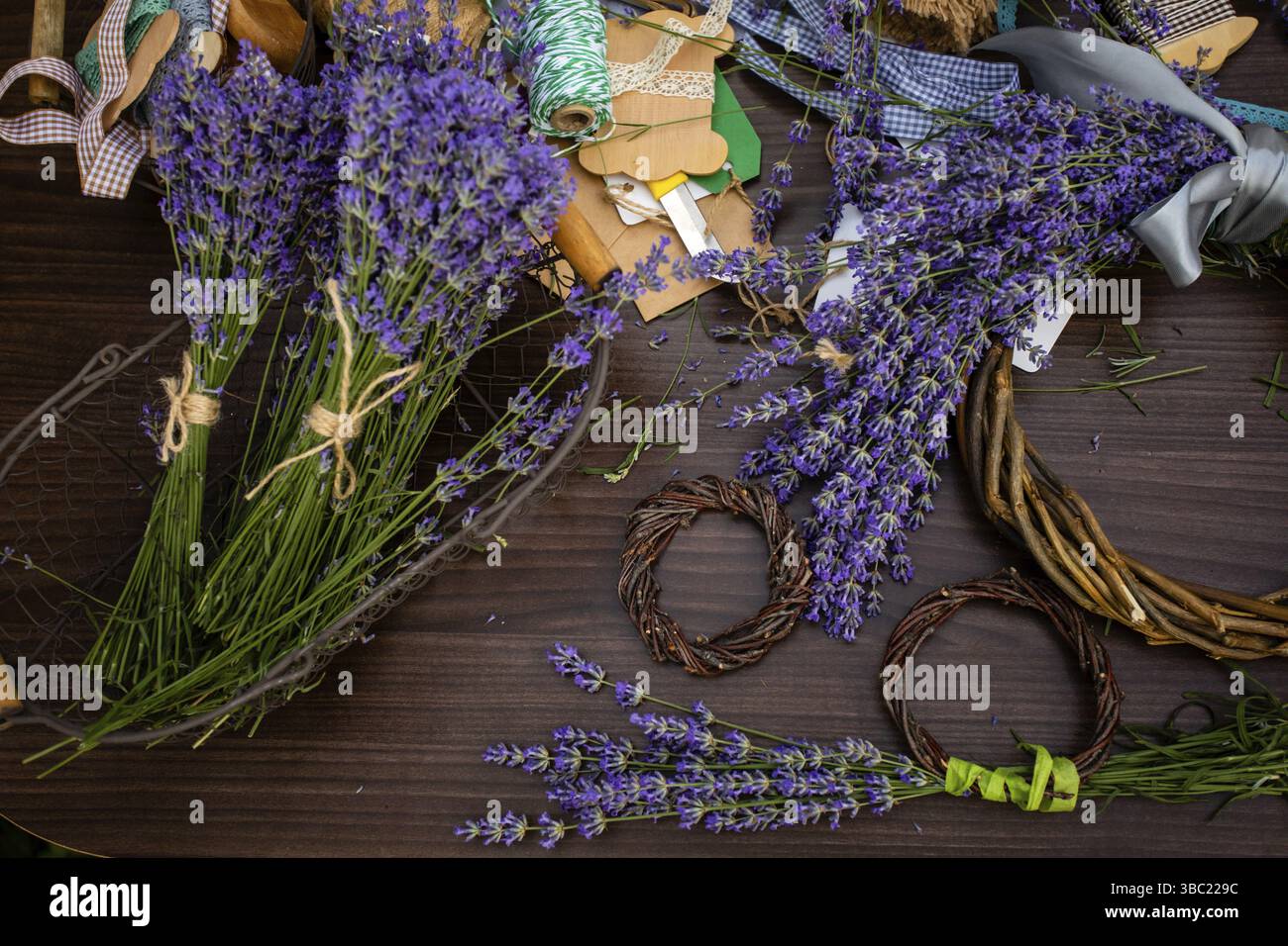 Gros plan bouquet de lavande fraîche placé dans un panier en métal. Variété d'accessoires et d'outils pour créer un décor artisanal lavande sur une surface en bois, b Banque D'Images