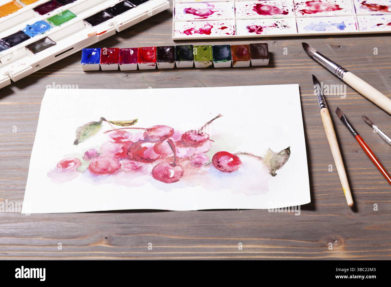 Œuvres d'art, peintures à l'aquarelle cerises avec outils de dessin sur une table en bois Banque D'Images