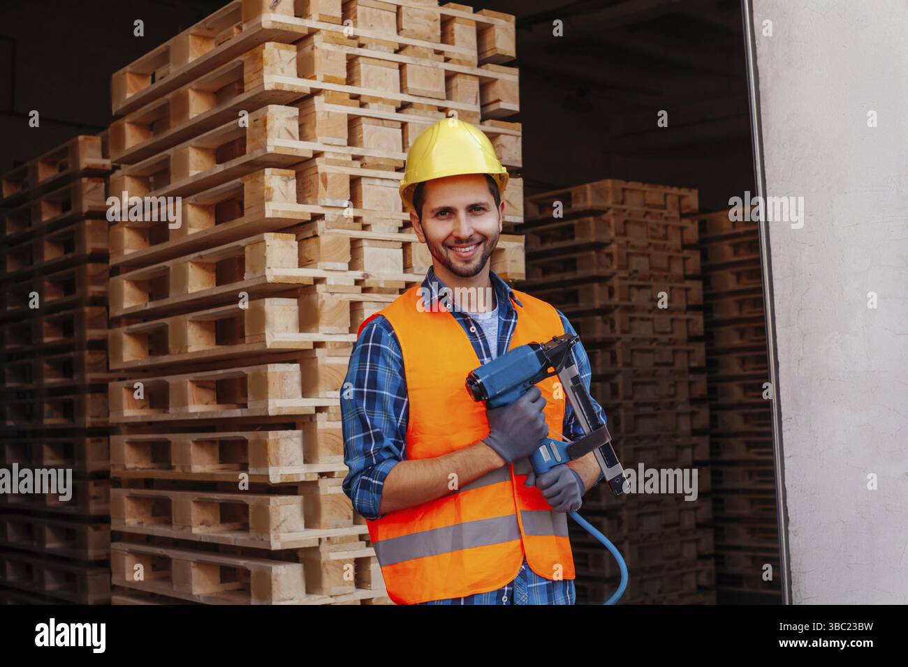 Portrait d'un jeune travailleur du bois professionnel, tenant un marteau pneumatique, posant sur une pile de palettes en bois de fond. Outils Indatrial dans les professionnels Banque D'Images