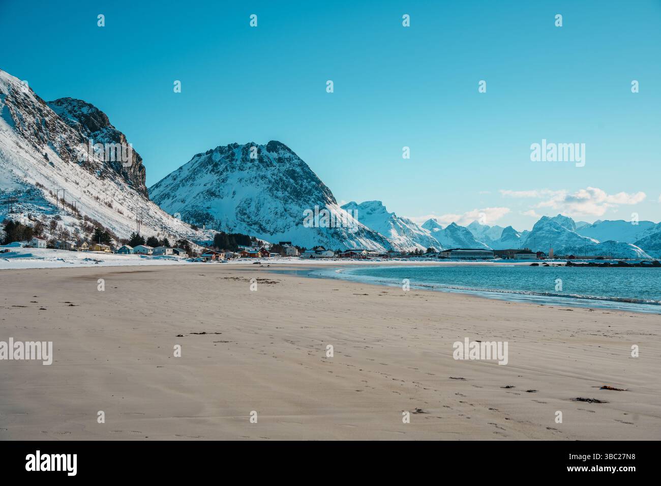 Paysage hivernal de Ramberg Beach sur l'île Lofoten, Norvège, avec rivage enneigé, eaux arctiques et sommets montagneux spectaculaires. Banque D'Images