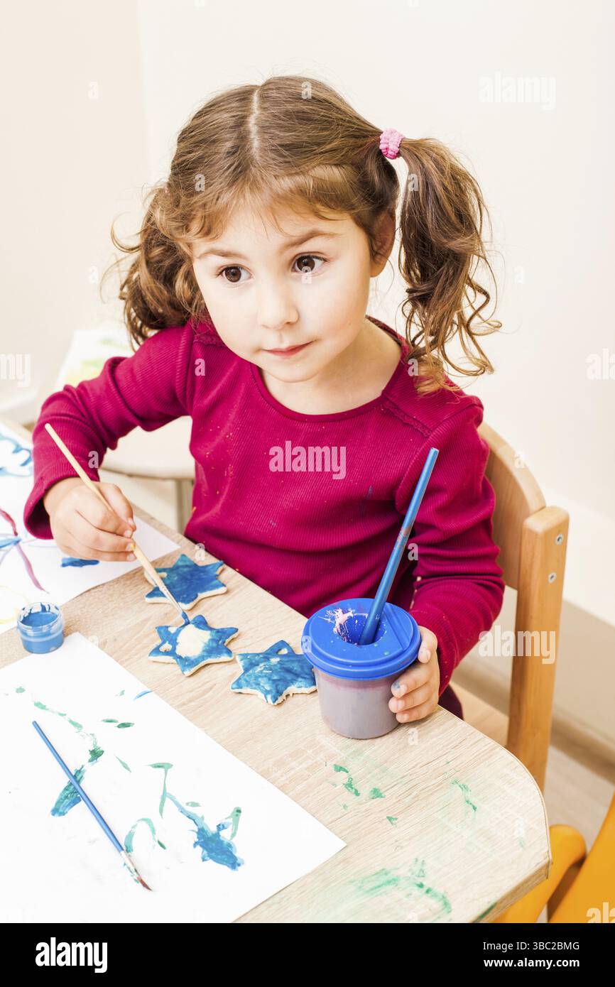 Fille, c'est peindre avec un pinceau et de la gouache sur un chiffres d'argile. Des décorations de noël faites à la main dans le jardin d'enfants Banque D'Images