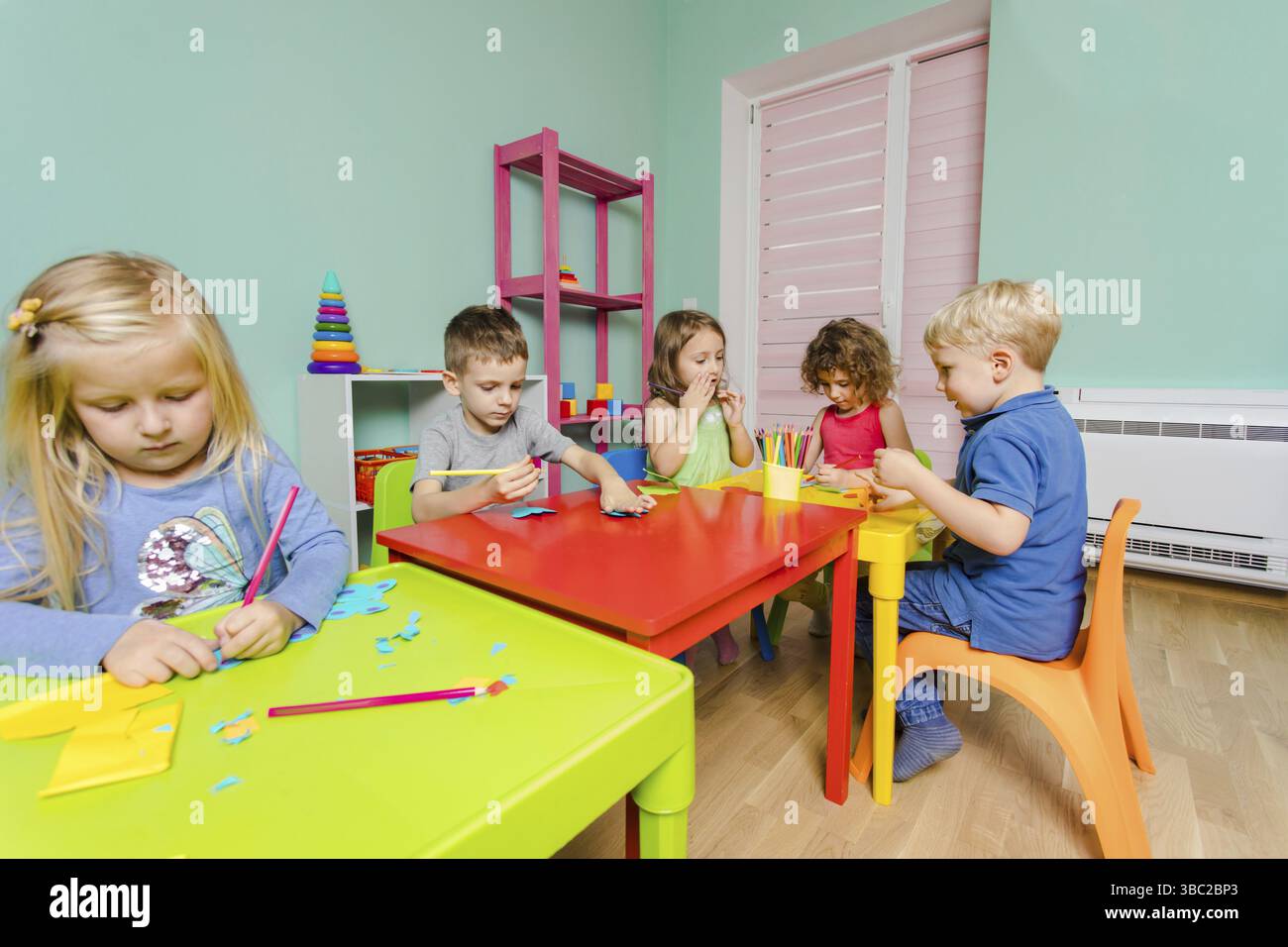 Les adorables enfants d'âge préscolaire s'assoient aux bureaux de la salle de jeux et dessinent avec des crayons de couleur Banque D'Images