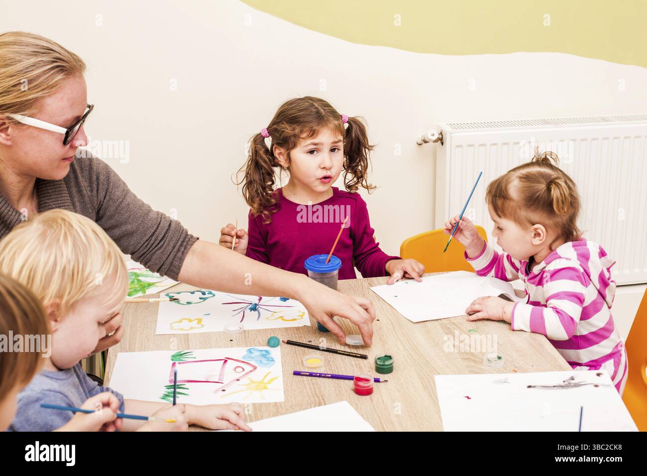 Les enfants et le tuteur sont la peinture à l'aide d'un pinceau et d'aquarelles sur papier dans le jardin d'enfants Banque D'Images