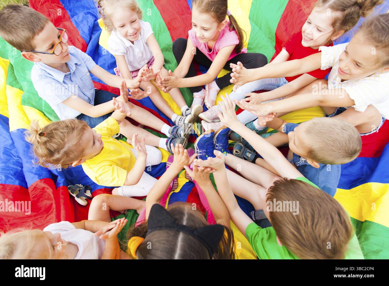 Groupe d'enfants assis dans un cercle mettant leurs mains ensemble, rire et s'amuser. Concept de camp d'été Banque D'Images