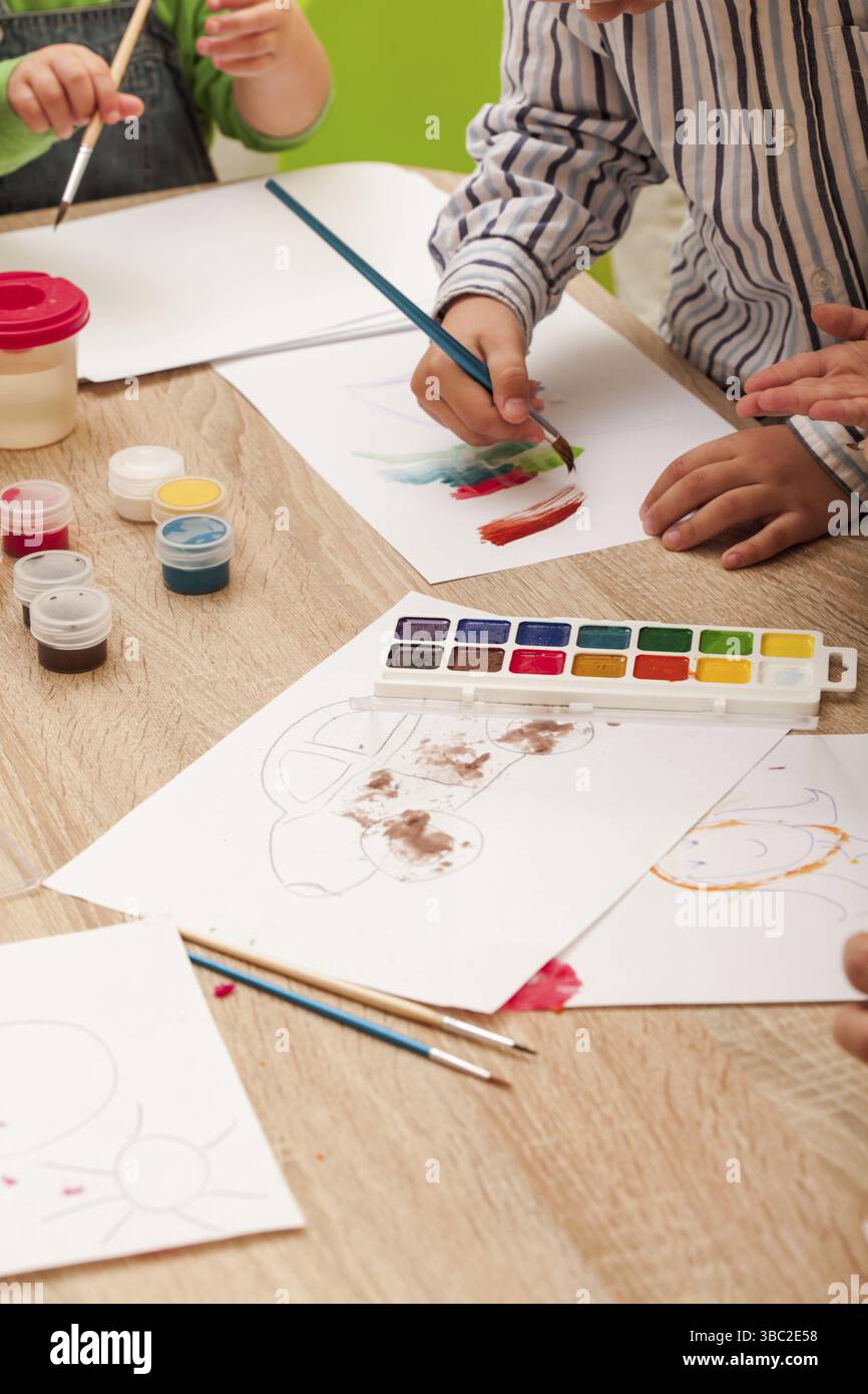 Les enfants apprennent à peindre avec un pinceau et des aquarelles sur papier à la maternelle Banque D'Images