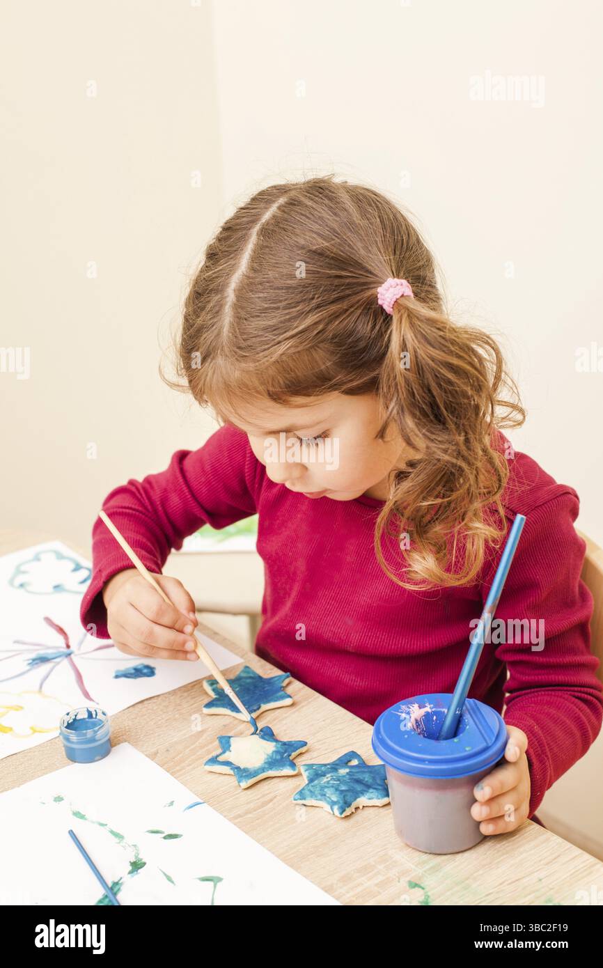 La fille peint avec un pinceau et des aquarelles sur des figures d'argile. Décorations de vacances faites à la main Banque D'Images