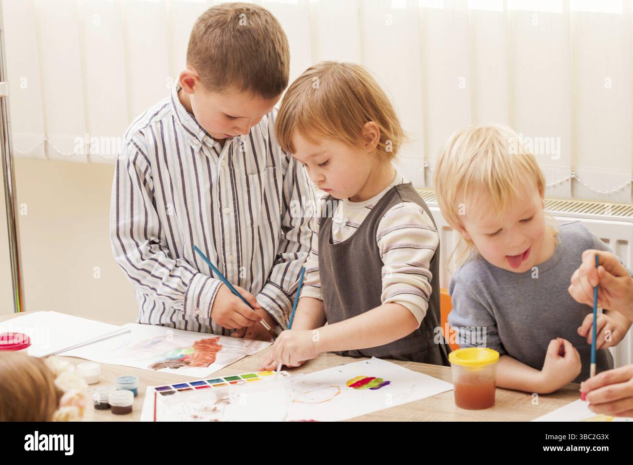 Les enfants apprennent à peindre avec un pinceau et des aquarelles sur papier à la maternelle Banque D'Images