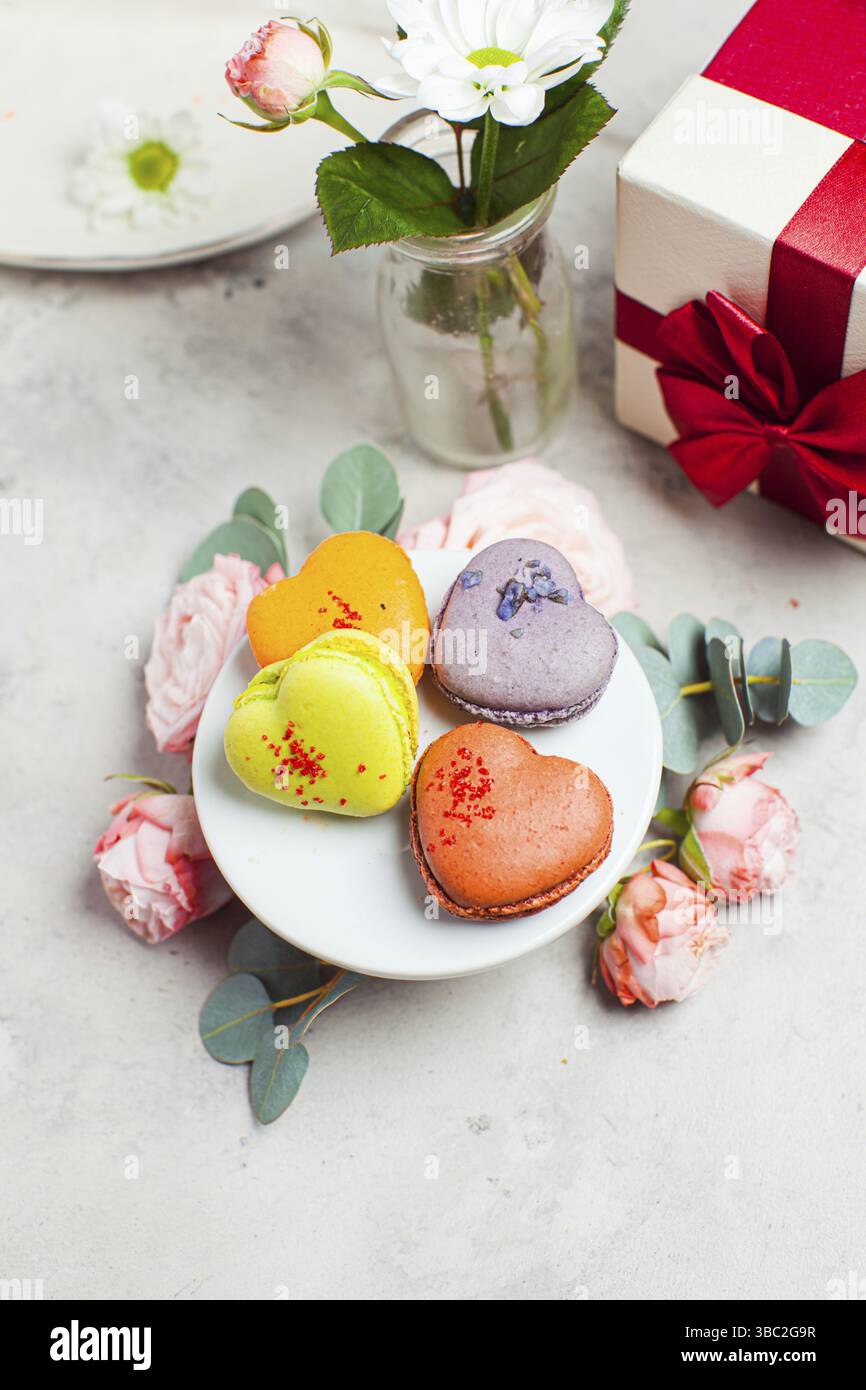 Ensemble de cupcakes colorés en forme de coeur disposés sur une table festive avec un bouquet de roses Banque D'Images