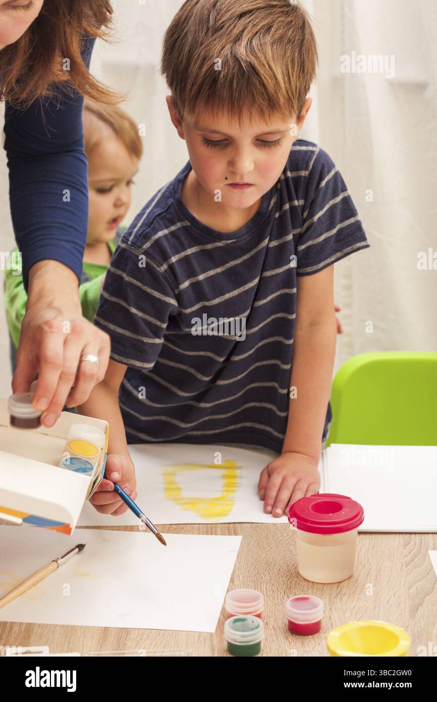 Les enfants apprennent à peindre avec un pinceau et des aquarelles sur papier à la maternelle Banque D'Images