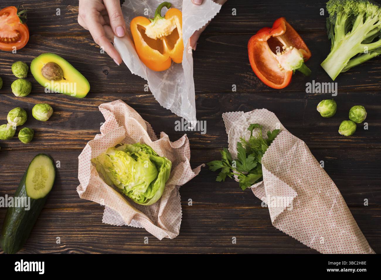 Vue de dessus des mains féminines enveloppant les légumes dans des enveloppements de cire d'abeille. Cuisine zéro déchet avec matériaux d'emballage réutilisés Banque D'Images