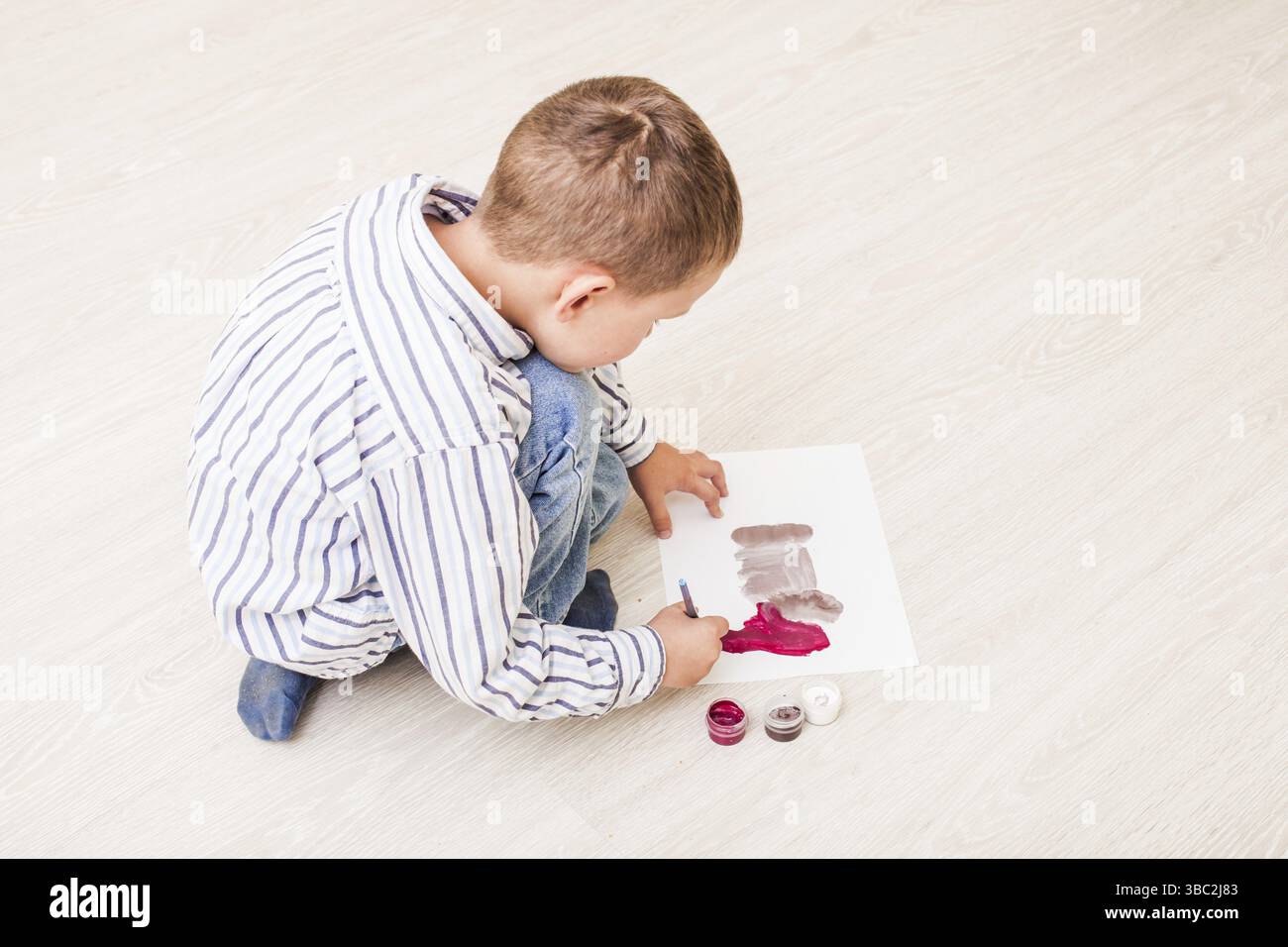 Boy est la peinture avec un pinceau et aquarelles sur papier sur le plancher Banque D'Images