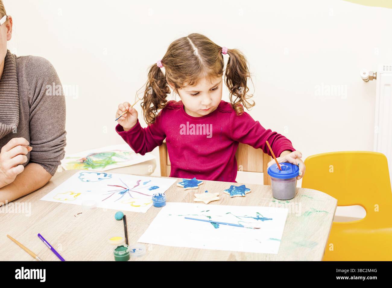 Fille, c'est peindre avec un pinceau et de la gouache sur un chiffres d'argile. Des décorations de noël faites à la main dans le jardin d'enfants Banque D'Images