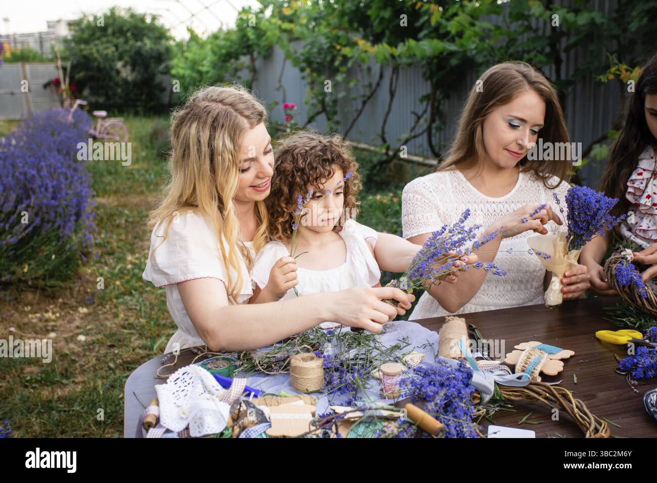 Portrait de la petite fille d'âge préscolaire prenant part à l'atelier. Table en bois avec couronne faite à la main décorée d'une belle fleur de lavande. Outils de fleuriste an Banque D'Images