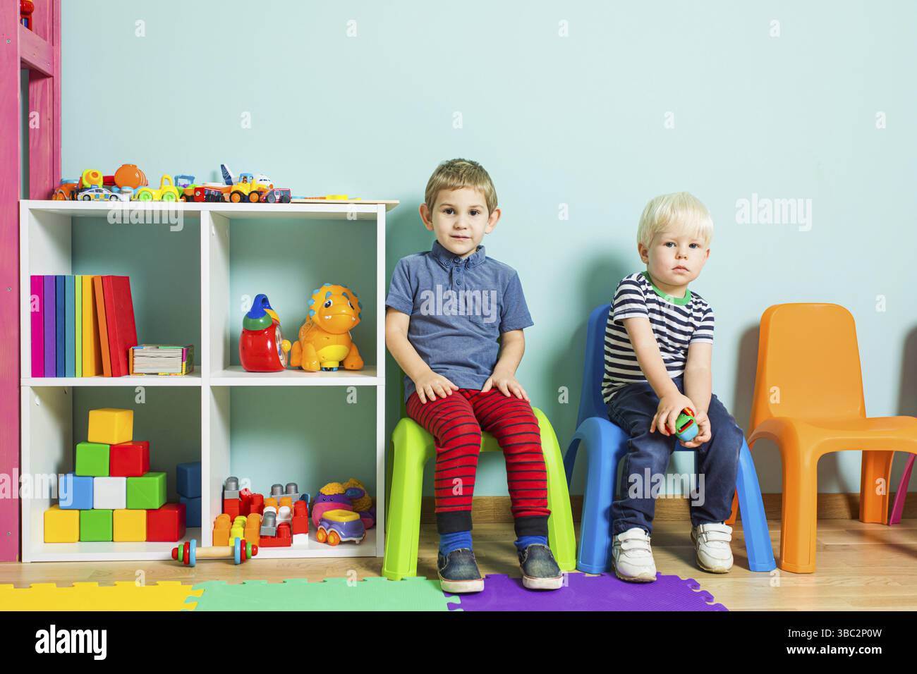 Deux garçons sont assis sur une chaise de couleur sur le fond du mur. Les enfants sont assis à la maternelle et regardent la caméra Banque D'Images
